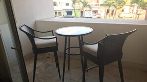 Un balcon avec deux chaises et une petite table ronde, d’où l’on peut admirer une rue et des bâtiments en arrière-plan.