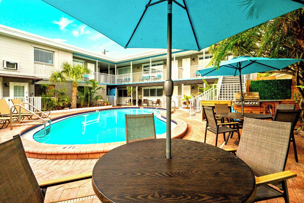 A pool area with a round table and chairs, a covered seating area, and a staircase leading to an upper level.