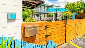 Un hotel de fachada blanca, valla de madera y zona de piscina con sombrillas.