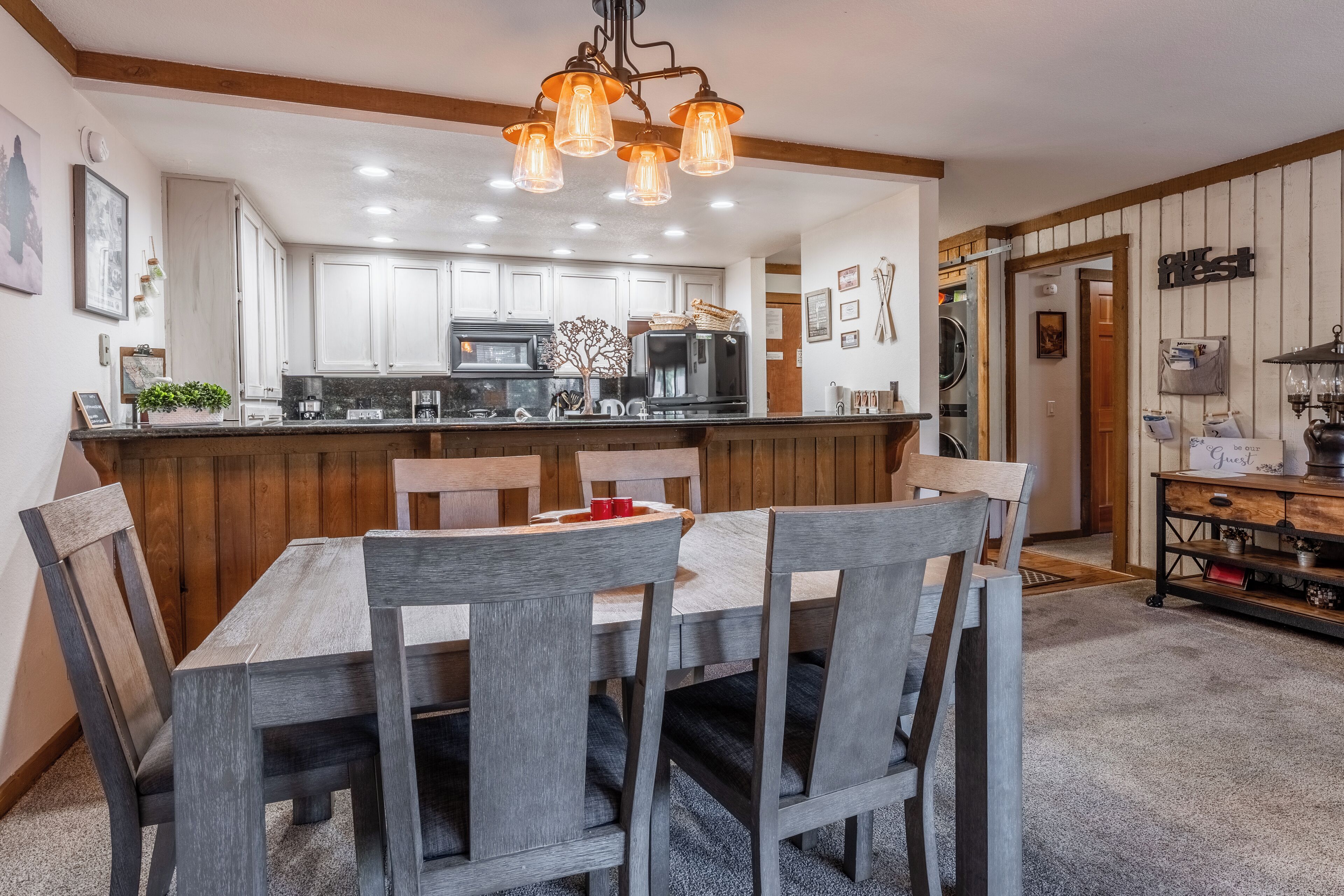 A modern kitchen with white cabinets, a central island, and a dining area with wooden chairs.
