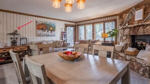 Uma sala de jantar acolhedora com mesa de madeira, cadeiras e uma tigela decorativa. Há uma pintura na parede e uma lareira com revestimento de pedra.