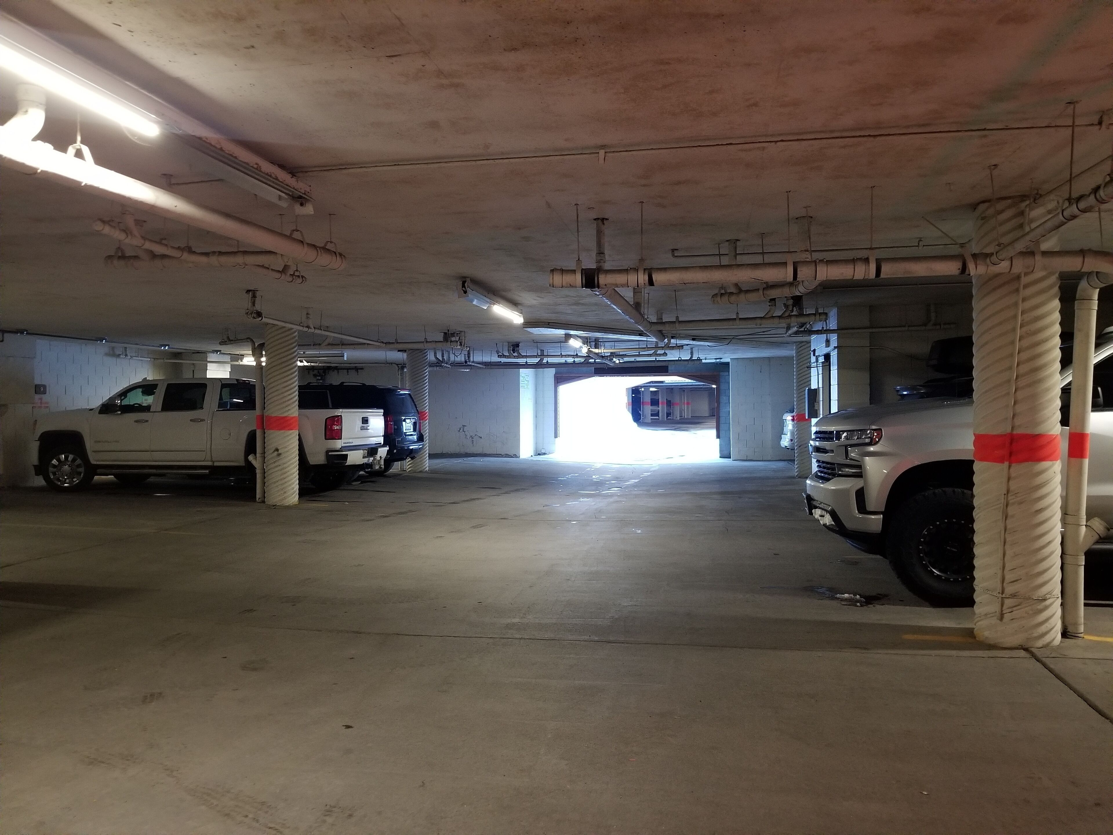 Un parking avec des piliers en béton, un éclairage fluorescent et deux véhicules stationnés.