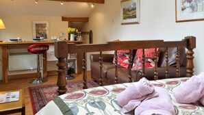 A cozy room with a bed, a wooden chair, a red stool, and a small table with a lamp. - A lovely open plan detached cottage in a rural location. (Near Sawrey, near Ambleside)