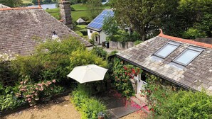 A garden with a patio, a white umbrella, and a house with a sloped roof and skylights. - A lovely open plan detached cottage in a rural location. (Near Sawrey, near Ambleside)