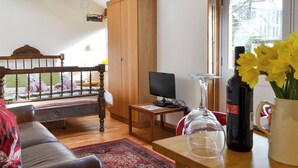 A cozy living room with a wooden bed, a television, a small table, and a window with flowers. - A lovely open plan detached cottage in a rural location. (Near Sawrey, near Ambleside)