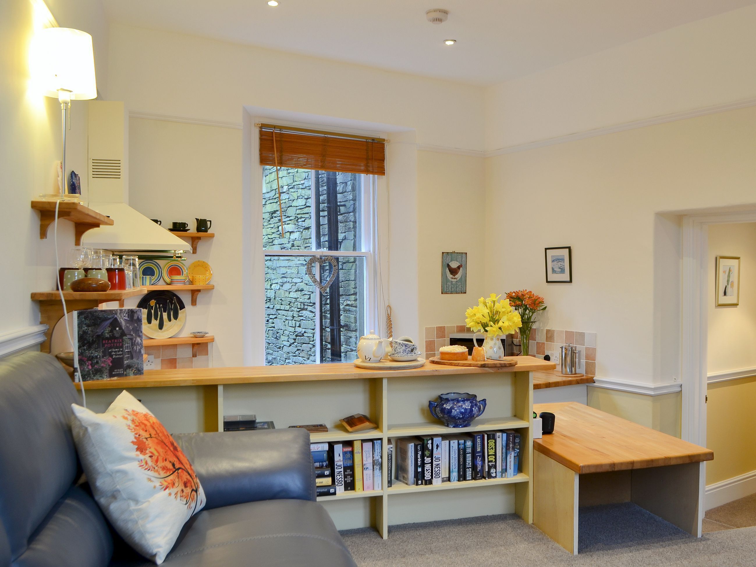 A cozy living room with a sofa, a coffee table, a bookshelf, and a window with a view of trees.