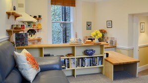 Un salon confortable avec un canapé, une table basse, une bibliothèque et une fenêtre donnant sur les arbres.