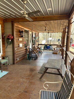 A covered outdoor patio with wooden benches and tables, a ceiling fan, and a view of the surrounding forest. - Anderson Paradise Cabin in Albert Pike Recreational Area, Caddo Gap Arkansas (Caddo Gap)