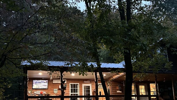 Eine Holzhütte mit einer Terrasse, einem Willkommensschild und einem Fernseher.