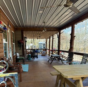 A covered porch with wooden furniture, a swing chair, and a picnic table. - Anderson Paradise Cabin in Albert Pike Recreational Area, Caddo Gap Arkansas (Caddo Gap)