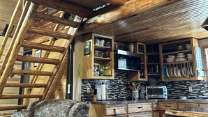 Ein rustikales Ferienhaus-Interieur mit Schlafzimmer im oberen Bereich, einer Holztreppe und einer Küchenzeile mit Holzausstattung und einer Mikrowelle.