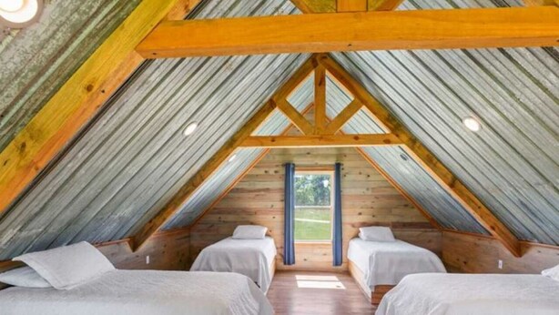 A cozy attic bedroom with two beds, wooden beams, and a view of the outdoors. - Private Country Getaway (Fitzpatrick)