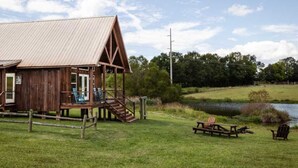 A rustic wooden building with a metal roof, a porch with chairs, and a picnic table by a pond. - Private Country Getaway (Fitzpatrick)