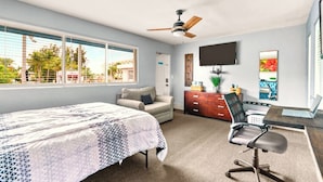 Une chambre à coucher avec un lit, un bureau et une chaise, un ventilateur de plafond et un téléviseur fixé au mur.