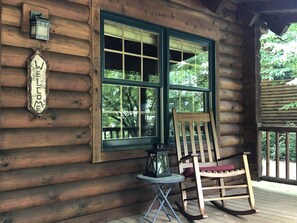 A wooden cabin with a large window, a rocking chair, a small table, and a lantern.