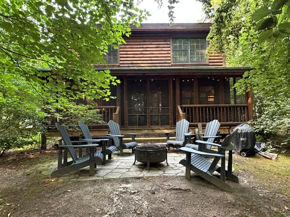A log cabin with a porch, outdoor seating, and a fire pit.