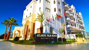 A multi-story hotel named Atlantic Palm Beach with a modern architectural design, featuring balconies and a well-maintained outdoor area with palm trees.