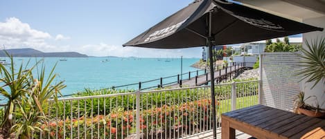 A balcony with a view of the sea, a wooden table, and a black umbrella.