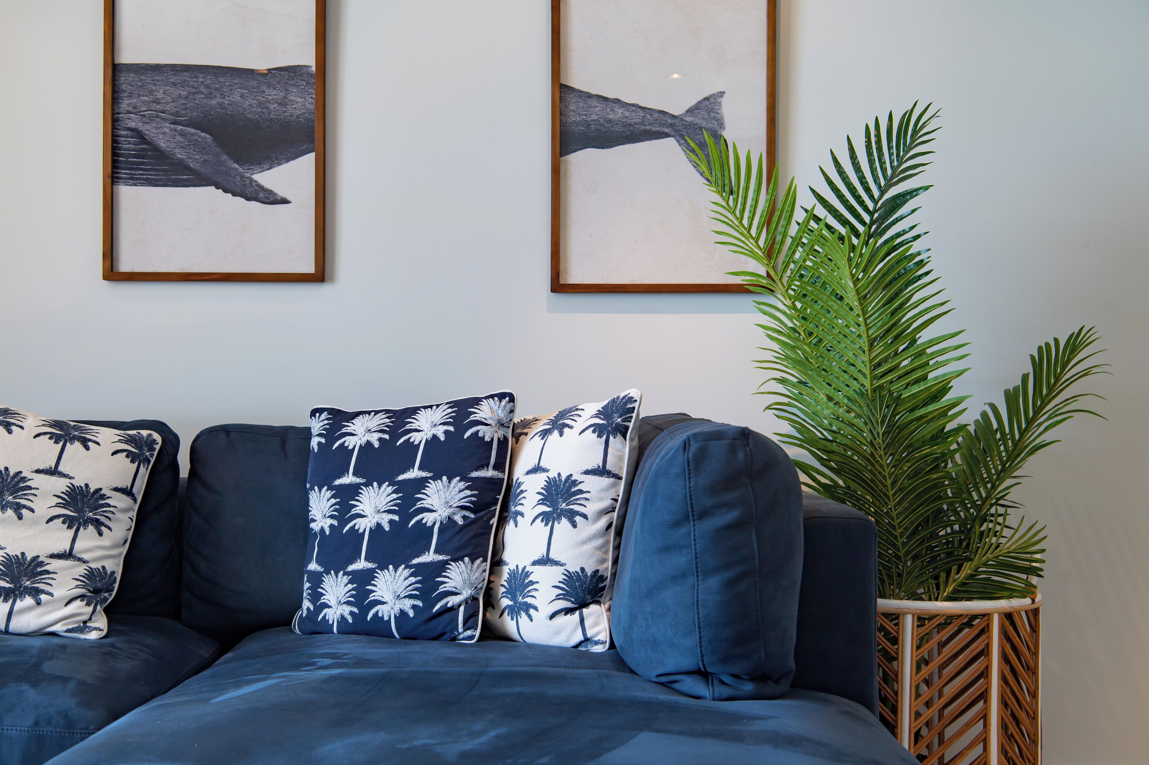 A modern living room with a dark blue sofa, three patterned pillows, and two framed whale paintings on the wall.