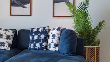 A modern living room with a dark blue sofa, three patterned pillows, and two framed whale paintings on the wall.