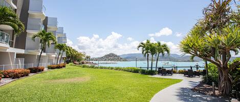 A hotel with a view of the ocean, a grassy area, and a seating area with tables and chairs.