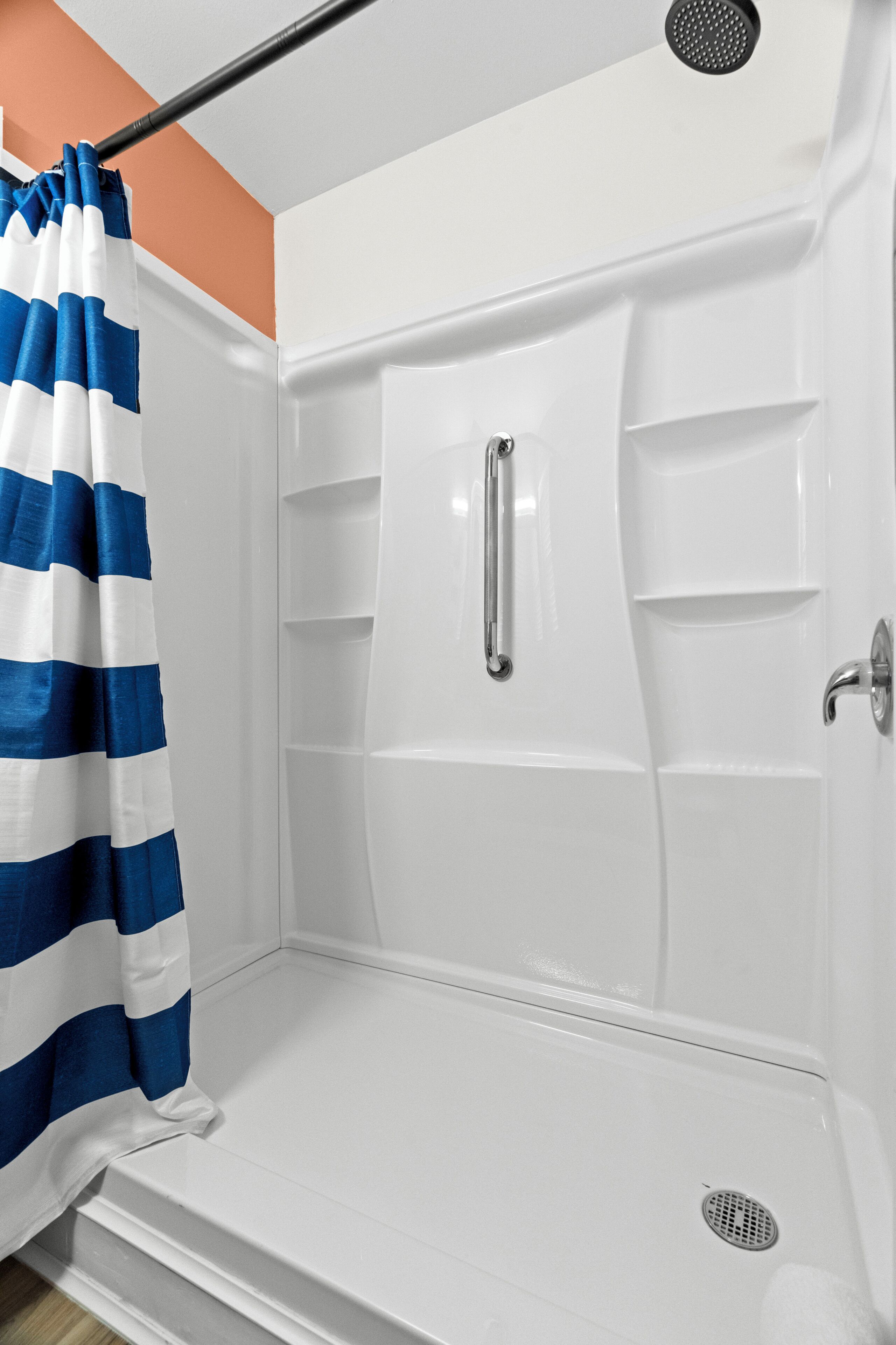 A shower enclosure with a white interior, a blue and white striped shower curtain, and a handrail.
