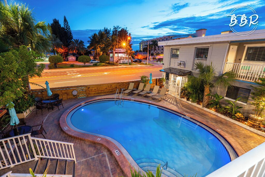 Une piscine à bordures courbes, entourée d’une terrasse en bois et accessible par un petit escalier menant à un balcon.