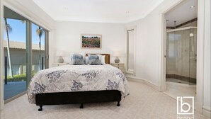 A bedroom with a large bed, a glass shower enclosure, and a view of palm trees. - Ocean views  Apartment within Resort - Star of the Sea - Heated Pool (Terrigal)