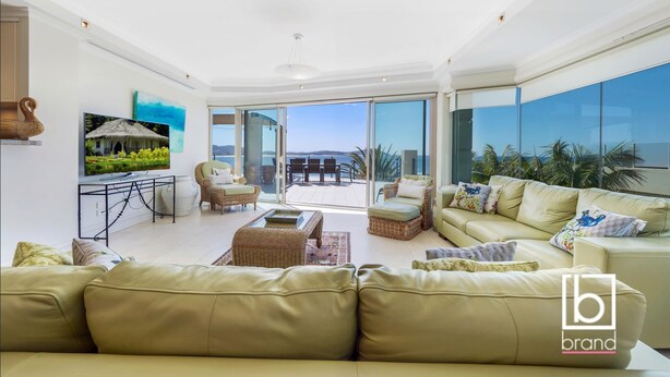 A spacious living room with a large sofa, a coffee table, and a TV on a stand. There is a balcony with a view of the sea. - Ocean views  Apartment within Resort - Star of the Sea - Heated Pool (Terrigal)