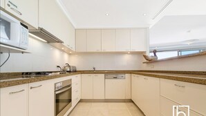 A modern kitchen with white cabinetry, granite countertops, a built-in oven, and a dishwasher. - Ocean views  Apartment within Resort - Star of the Sea - Heated Pool (Terrigal)