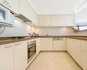 A modern kitchen with white cabinetry, granite countertops, a built-in oven, and a dishwasher.