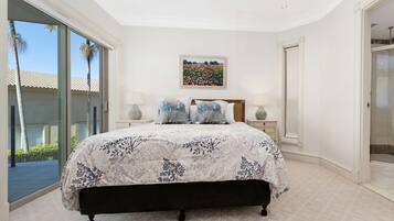 A bedroom with a large bed, a glass shower enclosure, and a view of palm trees.