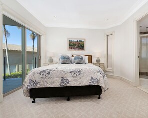 A bedroom with a large bed, a glass shower enclosure, and a view of palm trees.