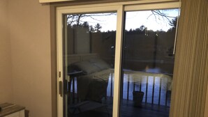 A room with a sliding glass door leading to a balcony with a view of trees and a fence.