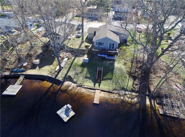 Vista aérea de una casa con jardín, un muelle y un bote pequeño.