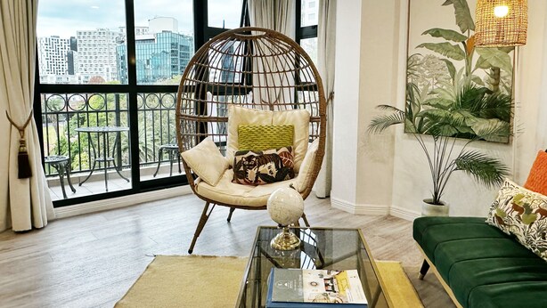 A modern living room with a large window, a hanging chair, a green sofa, and a glass coffee table with a book. - *Pool, spa, two balconies, park views!* (Auckland)