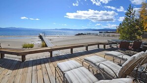 A wooden deck with outdoor seating overlooking a beach and ocean.