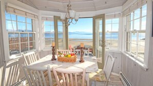 A sunlit dining room with a table set for two, overlooking a beach.