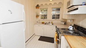 Una cucina compatta con mobili bianchi, un fornello, un forno a microonde e un frigorifero.
