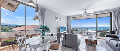 A modern living room with a dining area, large windows, and a view of the sea.