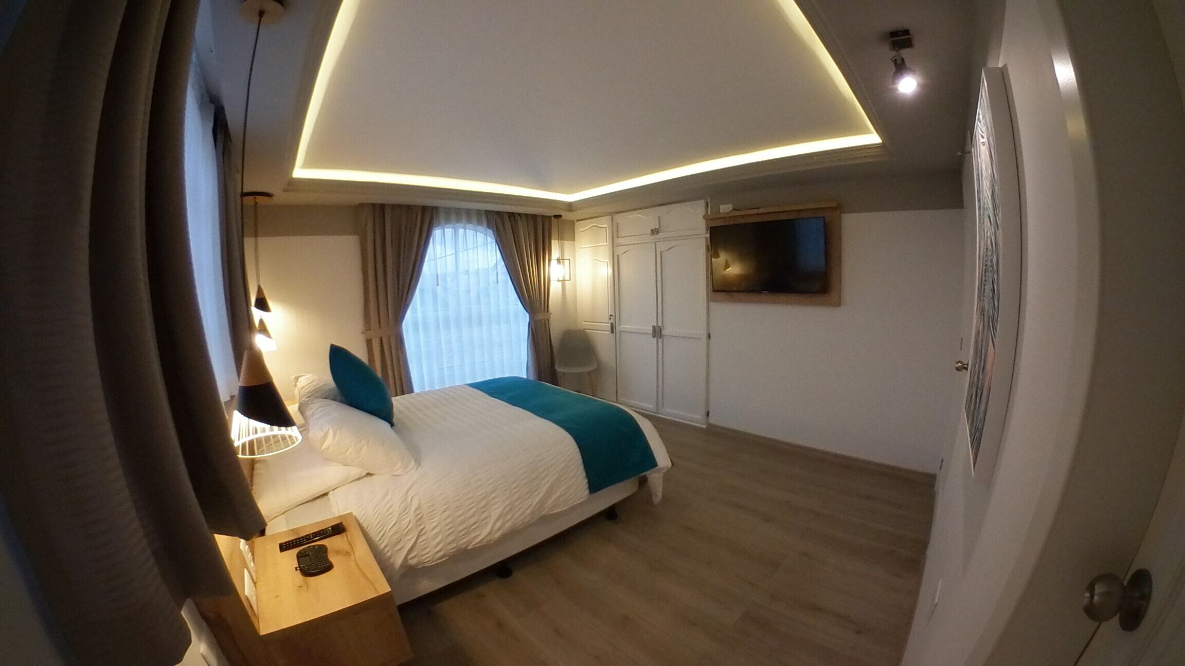 A modern bedroom with a bed, bedside table, and a TV mounted on the wall.