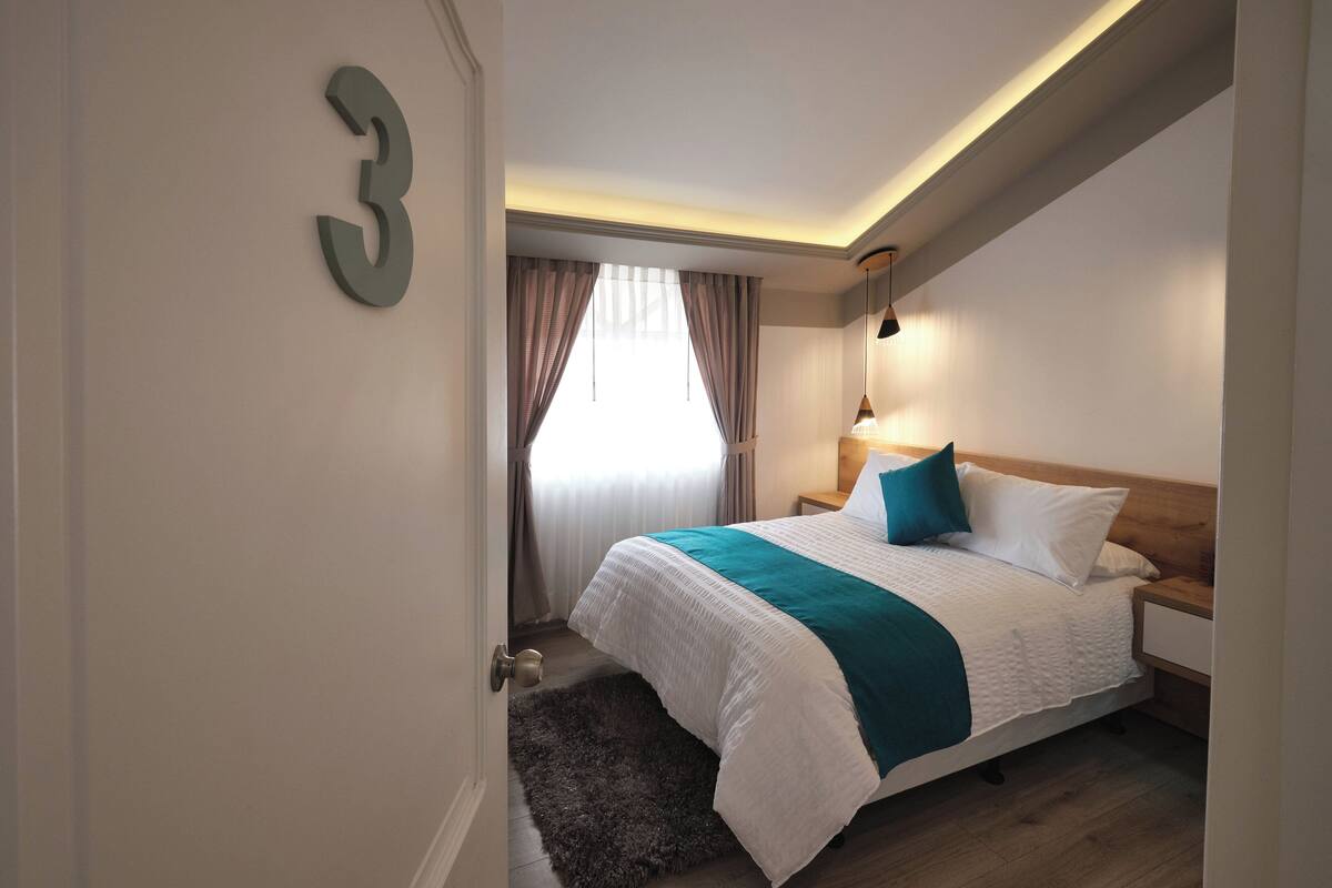 A hotel room with a bed, a nightstand, a lamp, and a number sign on the wall.