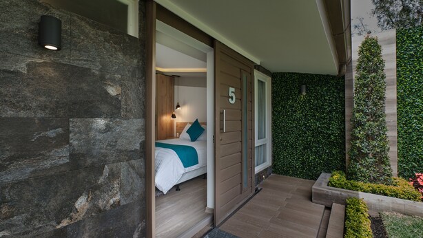 A modern hotel room with a stone facade, a bed with a teal accent, and a view of a green garden. - Asher Hospedaje y Turismo (Riobamba)