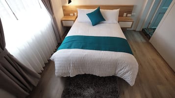 Una cama bien hecha con ropa de cama blanca y aguamarina, un cabecero de madera y una mesita de noche pequeña con una lámpara.