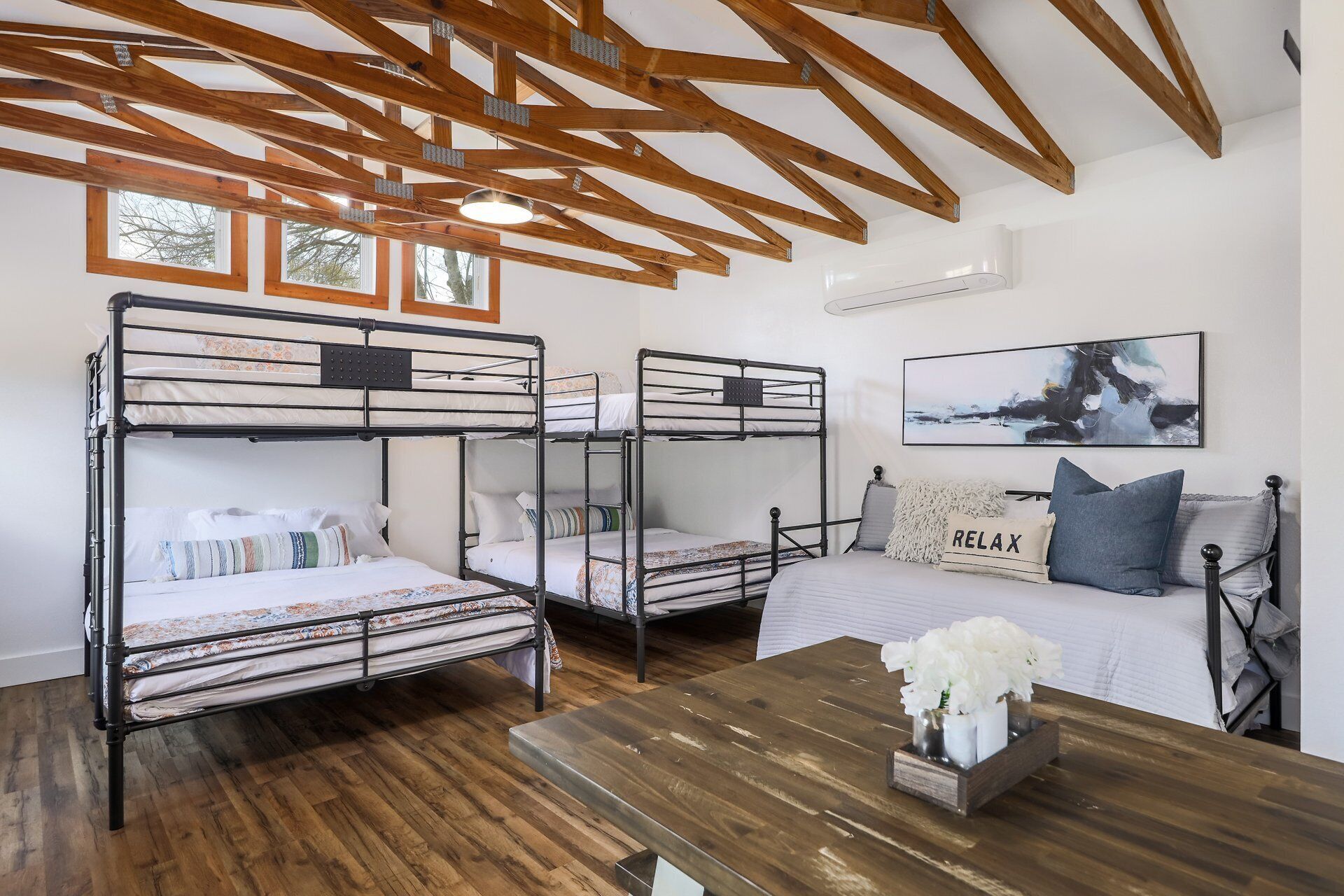 Ein Zimmer mit Etagenbetten, einer Holzbalkendecke, einem Gemälde und einem Tisch mit Blumen.