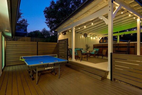 An outdoor patio with a ping pong table, seating area, and string lights. - South Austin Group Retreat with Swimspa and Backyard fun! (Austin)