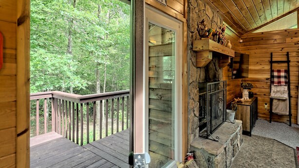 A wooden cabin interior with a glass door leading to a deck, a stone fireplace, and a shelf with decorative items.