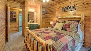 A wooden cabin bedroom with a bed, a dresser, a ceiling fan, and a wall-mounted bear decoration.