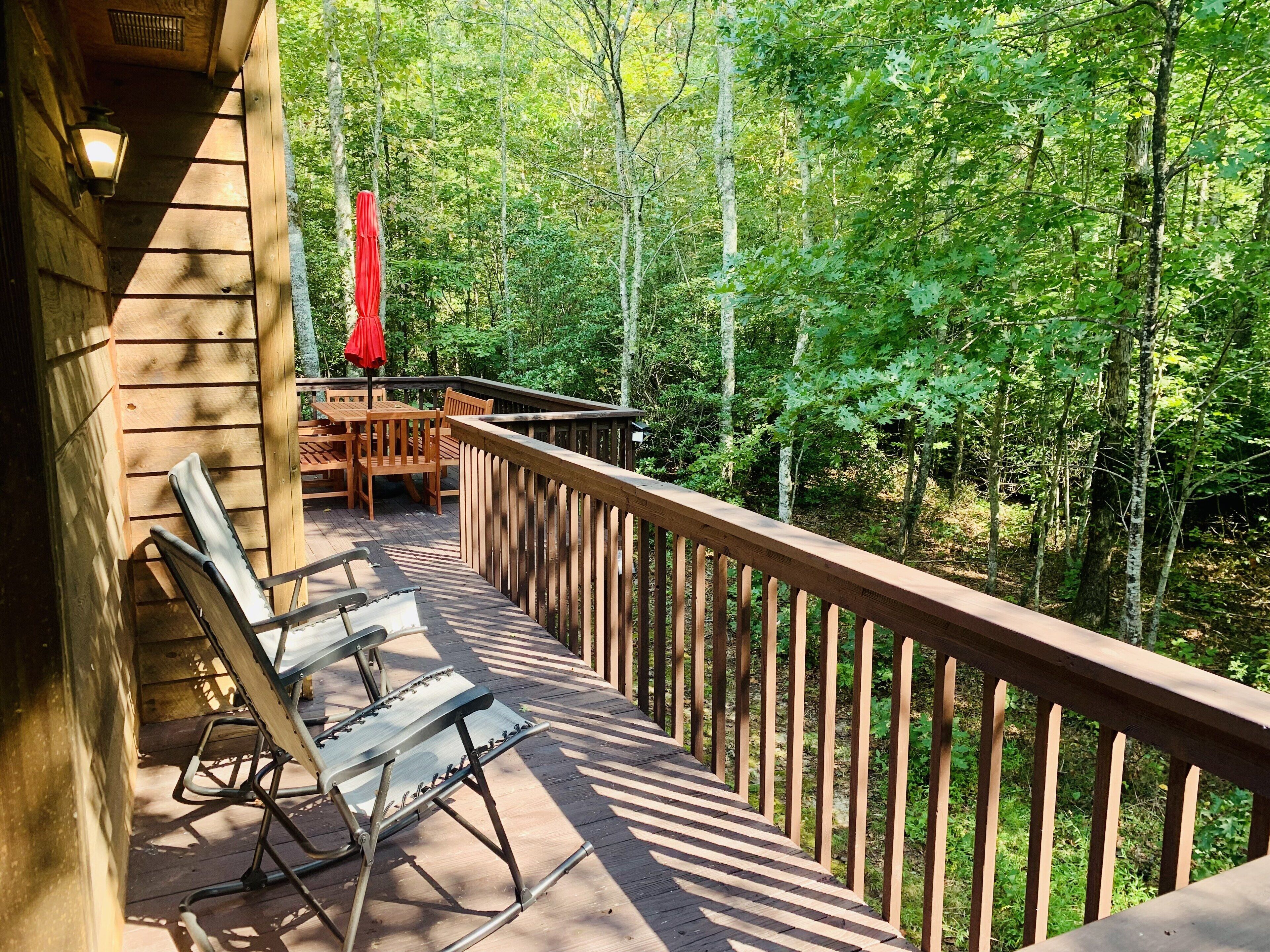 A wooden deck with a railing, a table with chairs, and a red umbrella.