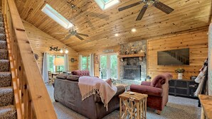 A cozy cabin interior with a wooden ceiling, a fireplace, a sofa, and a television.